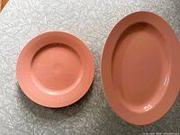 Top view of large round plate and oval serving platter, showing coral peach color and smooth surface.