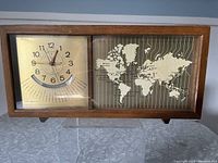 Full front view showing wooden frame clock with two panels: left with clock and time zone scale, right with world map and time zone lines.