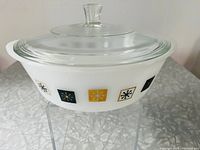 Front view of vintage white glass casserole dish with clear lid showing atomic snowflake pattern in colored squares around the side.