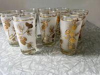 Eight frosted Libbey Dominion glasses with gold pinecone designs arranged on table.