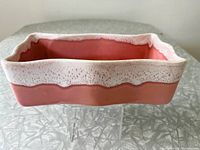 Photo showing the rectangular pink ceramic planter with white drip glaze around the rim, placed on a gray textured surface.
