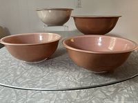 Four Pyrex Autumn Rainbow mixing bowls grouped on a glass surface, showing exterior colors and sizes.