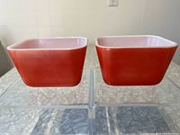 Two small red Pyrex refrigerator dishes shown side by side to display exterior red color and form