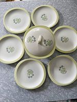 Overview photo showing six round plates arranged in a circle with the covered casserole dish in the center, all with yellow rims and floral decoration.
