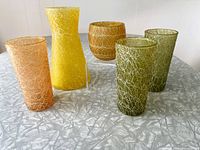 Five Spaghetti String glassware items including three tumblers, one roly poly glass, and one yellow vase arranged on table.