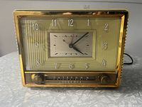 Front view of vintage Sylvania Art Deco bakelite clock radio showing gold-tone trim, rectangular clock face with Arabic numerals, and tuning dial below.