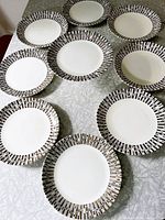 Nine vintage Crown Lynn Espresso Ironstone dinner plates arranged on a table, showing the geometric pattern on the rims with white centers.