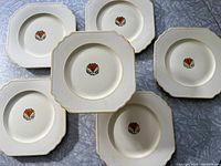 Six vintage Wedgwood cream plates with scalloped edges and red floral design in center, laid flat showing overall set condition and unique plate shape