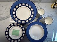 Photo showing dinner plates, salad plates with plaid design, and cups and saucers arranged on countertop to display set.