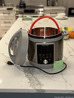 Front and angled view of Instant Pot with inner pot inside, showing control panel, lid open, and red handle of inner pot visible