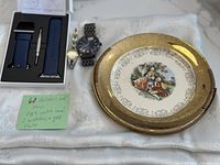 Overview of all items: Apple Watch band in box with tool, two wristwatches, and vintage gold-trimmed salad plate.