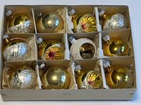 Full box of 12 vintage glass Christmas ornaments showing gold, silver, and white colors, all individually sectioned with cardboard dividers and tissue paper.