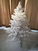 Front view of a 3-foot white artificial Christmas tree with multiple layers of full, spread out branches and plastic tripod base in indoor setting.