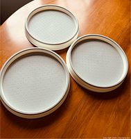 Three round light gray Lazy Susan trays with non-slip surfaces on a wooden table.