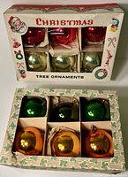 Two original boxes containing 12 large glass Christmas ornaments in red, green, orange, and light green.