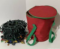 Four rolls of string lights coiled tightly with multi-colored bulbs visible alongside a red and green fabric carry case with straps.