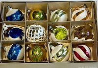 Top-down view of all 12 vintage glass ornaments in box compartments showing varied colors and decorations.