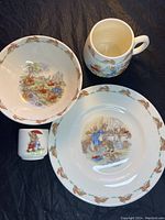 All four ceramic pieces: plate, bowl, mug, and small cup, showing their detailed Bunnykins illustrations and patterned rims.