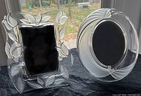 Both embossed glass picture frames together, showing distinct embossed leaf and floral pattern on rectangular frame and smooth oval frame with some detailing.