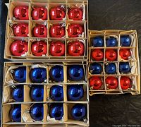 Three cardboard boxes containing blue and red vintage glass Christmas ball ornaments arranged in compartments with tissue paper.