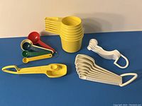 Yellow vintage Tupperware stacking measuring cups and sets of measuring spoons including white handled, yellow handled, and multicolored plastic spoons laid out on a blue background.