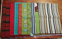 Top view of nine colorful placemats laid side by side horizontally showing various patterns and colors including stripes, textured fabrics, and floral applique flowers.