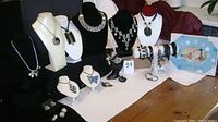 Full display of lot items showing necklaces on busts, bracelets on stands, rings on ring holders, earrings and baby boy picture frame on table.
