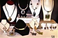 Photo showing the collection of costume jewellery including necklaces on display busts, earrings, rings, and a metal bracelet with rectangular brown faux stone.
