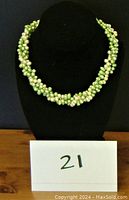 Full view of the necklace displayed on a black bust stand, highlighting its three-strand braided design of green and cream freshwater pearls.
