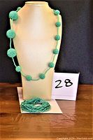 Turquoise beaded necklace displayed on a stand alongside a turquoise beaded bracelet laid flat.