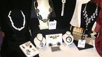 Display of various costume jewellery on black and white stands including necklaces, bracelets, brooches, earrings, and hairclips