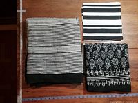 Three folded fabrics: striped napkin, floral patterned shawl, and floral patterned tablecloth all in black and white