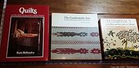 Front cover image of three hardcover books about traditional textiles: 'Quilts' by Ruth McMendry, 'The Comfortable Arts' by Dorothy K. Burnham, and 'Plain Nancy'.