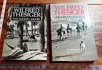 Two hardcover books by Wilfred Thesiger, "The Marsh Arabs" and "Arabian Sands", shown side by side on a wooden surface with measuring tape visible.