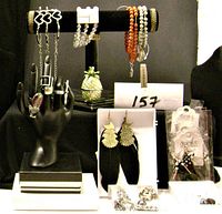 Set of jewelry displayed on hand display, T-bar, with pineapple trinket box visible behind, showing various bracelets, rings, earrings, and brooches arranged.