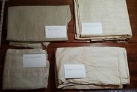 Four folded fabric remnants labeled as silk (?), beige, rough woven, and hemmed white cotton on wooden surface.