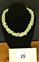 Front view of the necklace displayed on black bust showing the full three-strand woven design and color tones of green and yellowish pearls.
