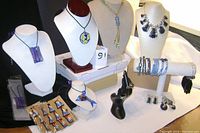 Photo showing the full collection of jewelry with necklaces on busts and bracelets displayed on a bar, rings on displays, and magnets arranged on cards.