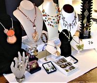 Photo showing 12 necklaces on display busts, multiple bracelets laid out, earrings on hand and trays, and two pendants