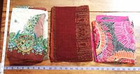 Three scarves/shawls laid side by side: left is paisley with brown base, center is solid maroon with pattern, right is bright silk floral in pink and orange.