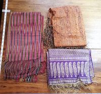 Photo of all three shawls folded on wood surface with measuring tape for size reference.