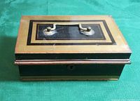 Top angled view of vintage painted metal cash box showing rectangular decorative borders and metal handle on top