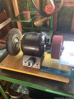 Side view showing black motor housing, red polishing wheel on one side, and wire brush wheel on the opposite side mounted on a yellow base.