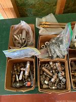 Various brass and metal pipe fittings, valves, nuts, and bolts packed in boxes and plastic bags displayed on a green table.
