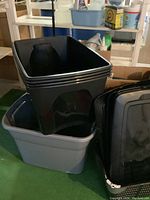 Photo of stacked black and gray plastic storage bins and lids.