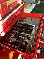 Opened red tool chest drawer showing various drill bits, tap and die tools arranged horizontally.