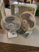 Two Super brand pedestal fans and one Electrohome vintage box fan in basement setting.