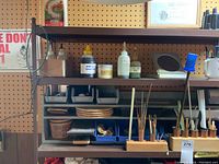 Shelf with various bottles of oils, containers, wooden paintbrush holder with brushes, small bins, and craft supplies.