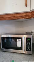 Front view of Hamilton Beach microwave on kitchen counter showing chrome and black finish, digital display, and control panel.