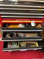 Open toolbox drawers revealing assorted hand tools including hammers, wrenches, socket set, hacksaw, and belts.